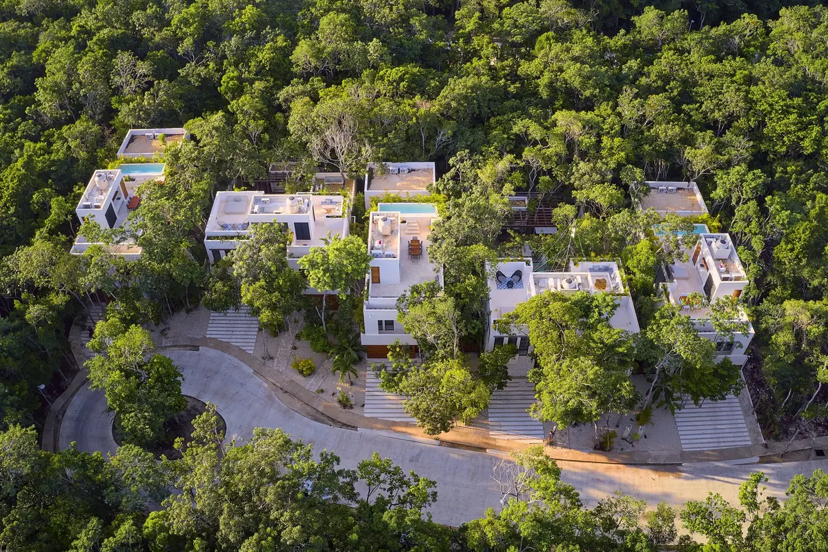 Aerial view of the five white Aldea Kaan Tulum villas with rooftop pools beside a curved road in the jungle of La Privada