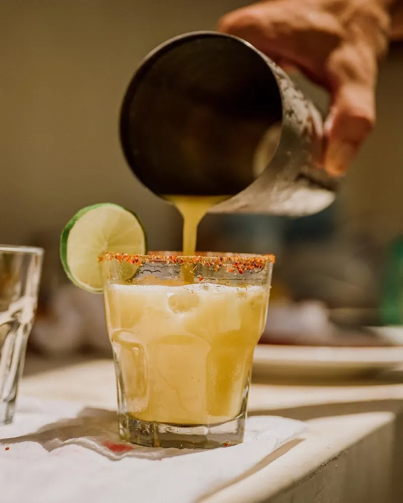 A cocktail poured from a shaker into a glass with a chili salt rim and a lime wheel