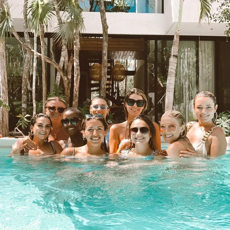 Nine guests in the pool in front of an Aldea Kaan Tulum villa with glass walls and palm trees