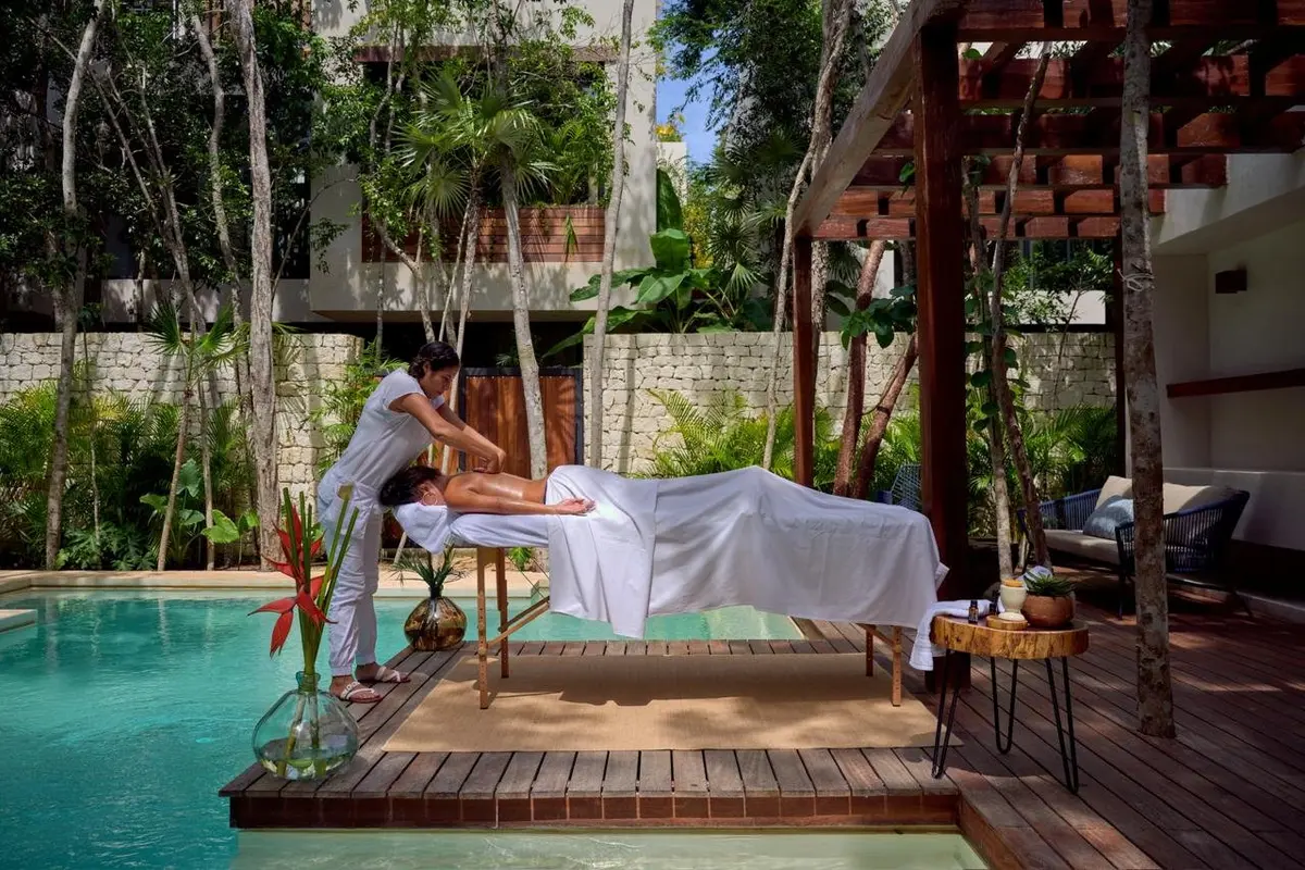 A massage on a wooden deck beside the pool of an Aldea Kaan Tulum villa, under a pergola