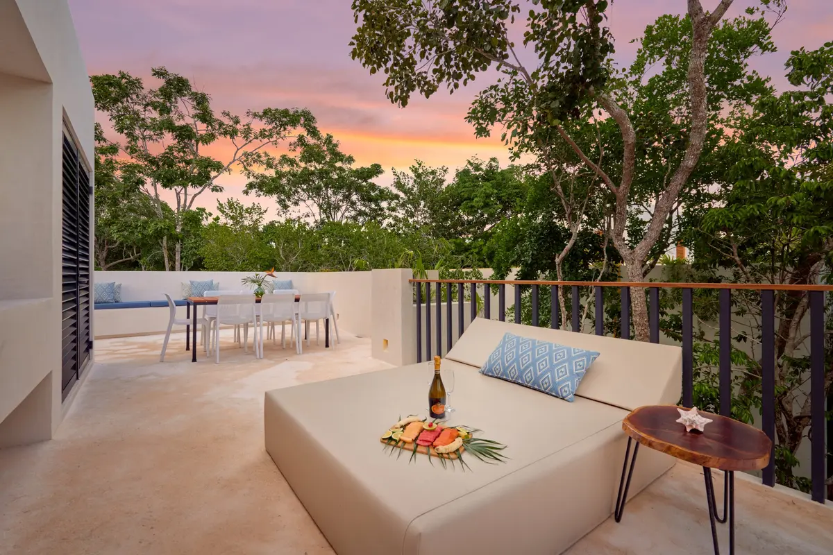 The Casa David rooftop terrace at sunset: a daybed with a bottle of sparkling wine and a fruit plate, and the dining table behind