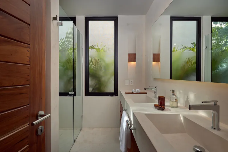 Casa David bathroom with a double sink vanity, wide mirror, glass shower and frosted windows