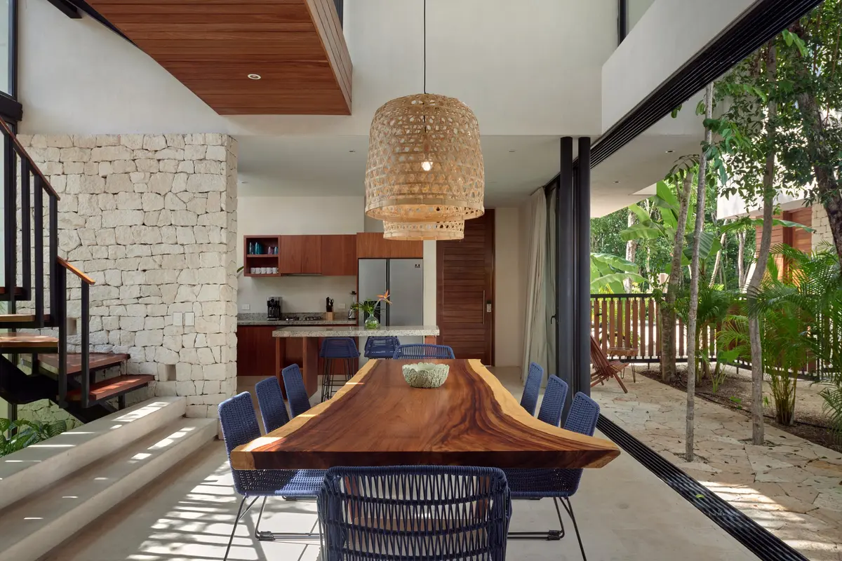 Casa David double height dining area and kitchen with a live edge table, blue chairs and glass doors open to the garden