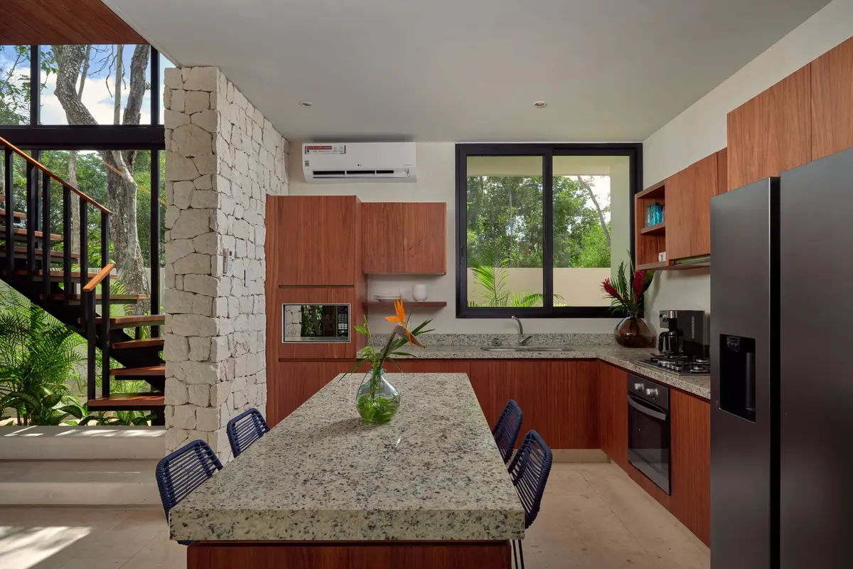 Casa David kitchen with a granite island bar and four blue stools, wooden cabinets and a stone wall beside the open staircase
