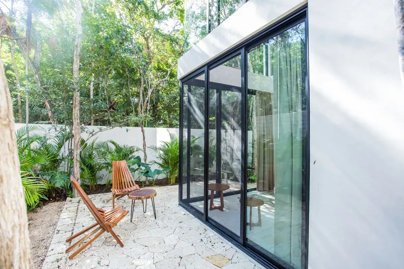 Casa David loft patio with two wooden folding chairs and a round side table on the stone paving beside the loft's glass sliding doors, with palms along a white garden wall