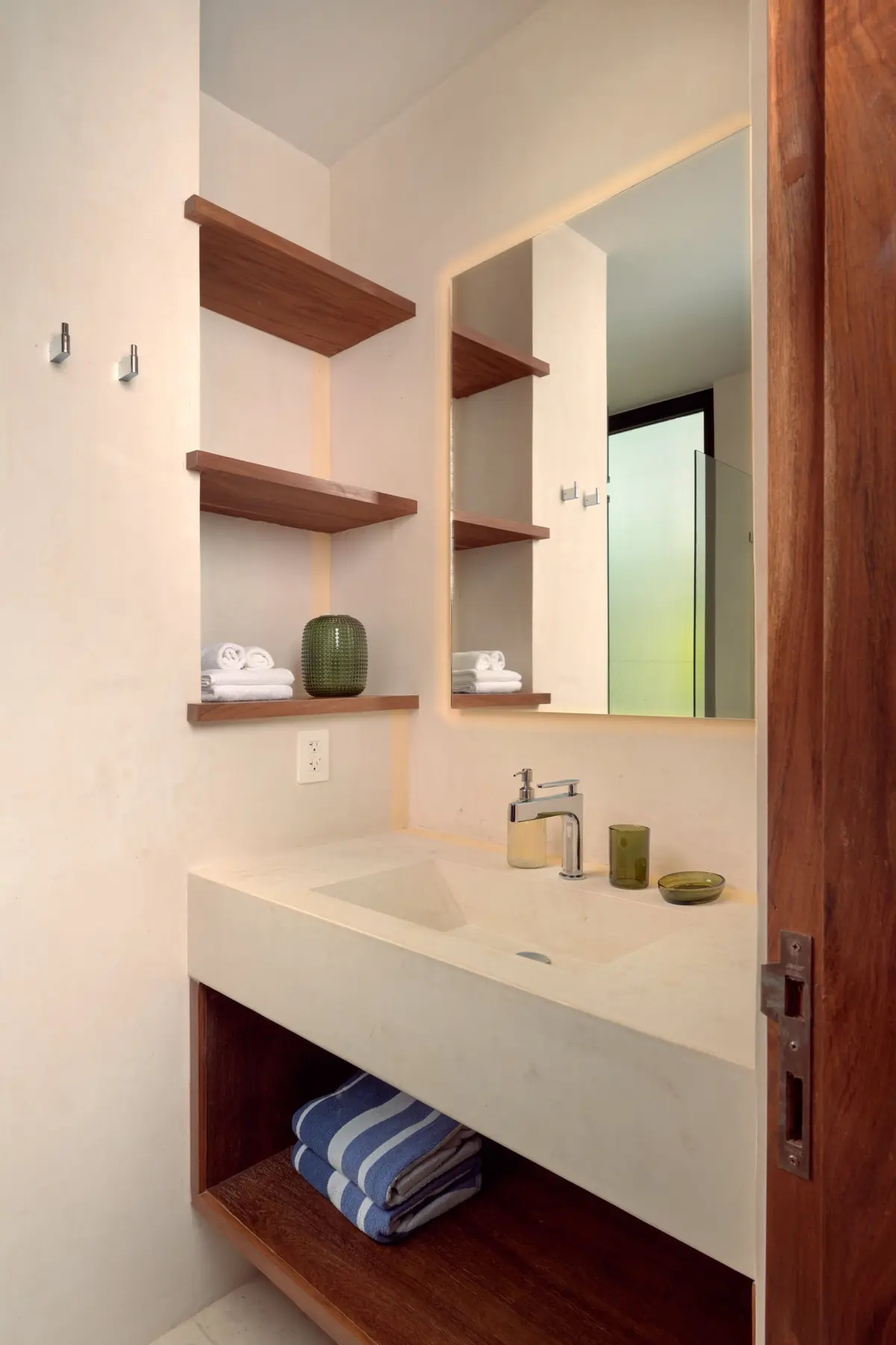 Casa Emilia bathroom with a white stone sink, wooden shelves and folded striped towels