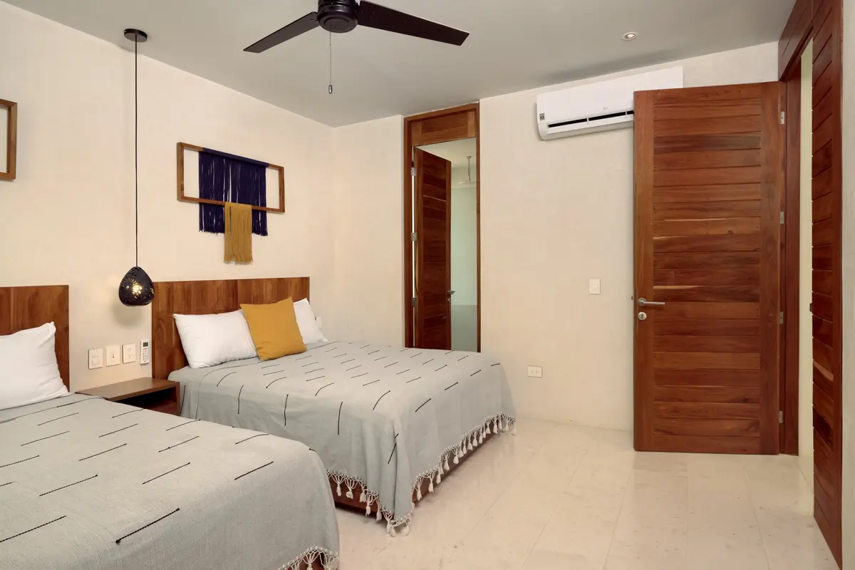 Casa Emilia bedroom with two beds in grey coverlets, a framed wall hanging and wooden doors