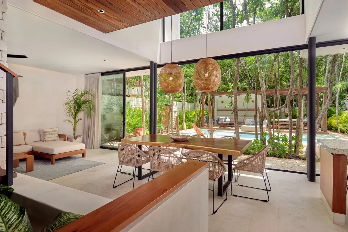 Casa Emilia open plan dining and living area with a wooden table, woven pendant lamps and glass walls onto the pool