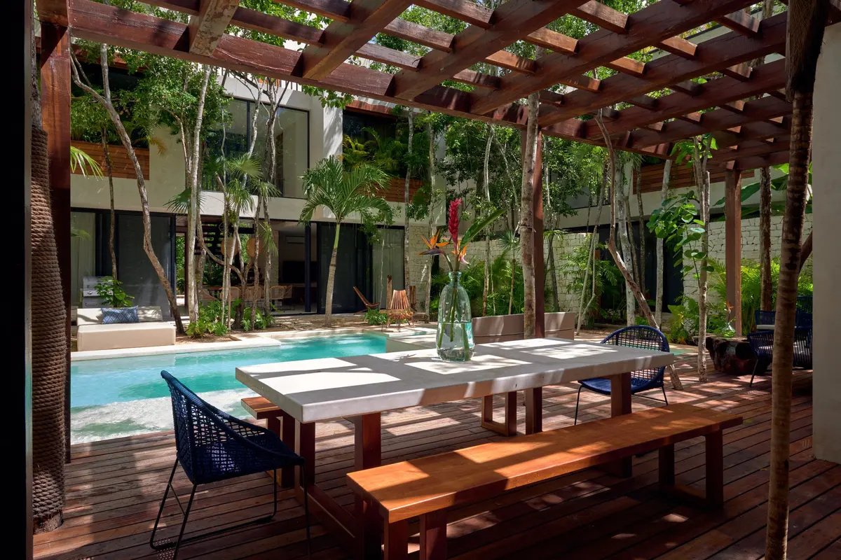 Casa Emilia outdoor dining table under a wooden pergola beside the pool with the house behind