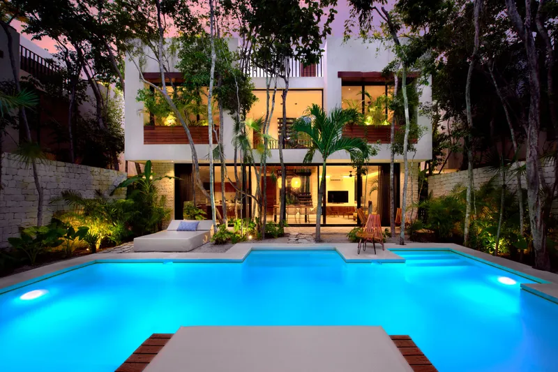 Casa Emilia swimming pool lit at night in front of the house with glass walls and palms