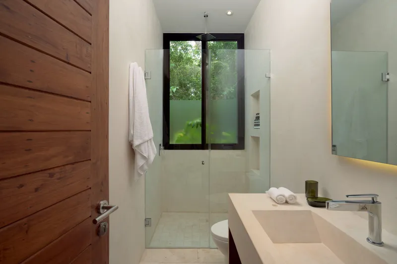 Casa Lucas bathroom with a glass shower under a window, a stone vanity and a wooden door