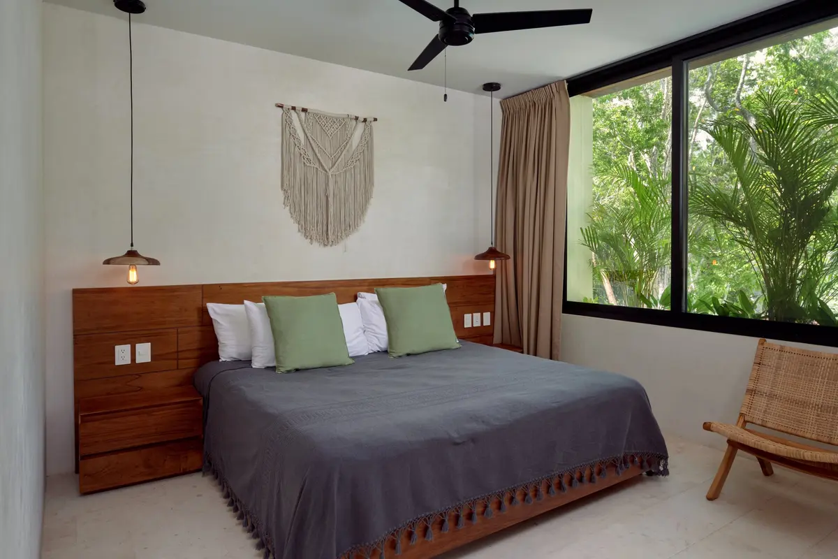 Casa Lucas bedroom with a wooden headboard, green pillows, macrame wall hanging and a window onto palms