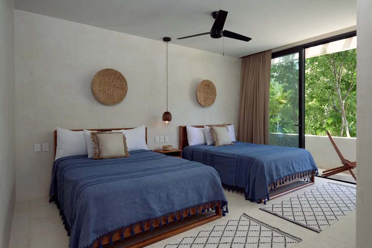 Casa Lucas bedroom with two beds in blue coverlets, woven wall discs and a door open to a terrace