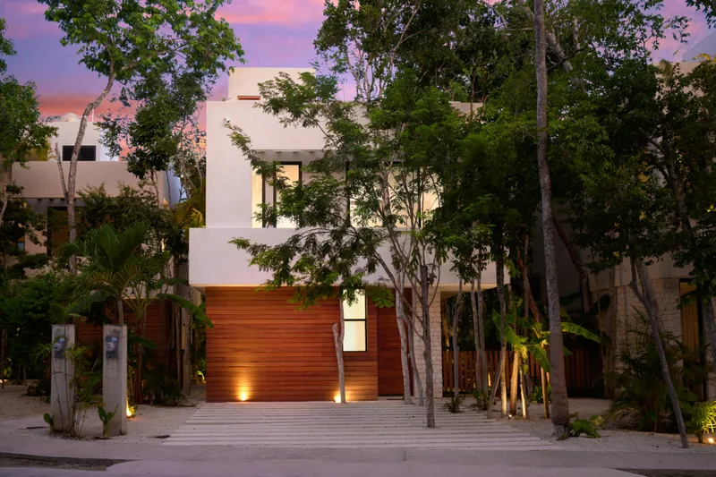 Casa Lucas facade from the street at dusk with a wood clad ground floor and tall trees