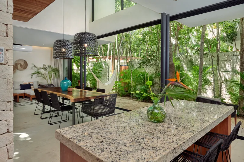 Casa Lucas kitchen counter with bar stools, a dining table with black chairs and glass walls onto the garden