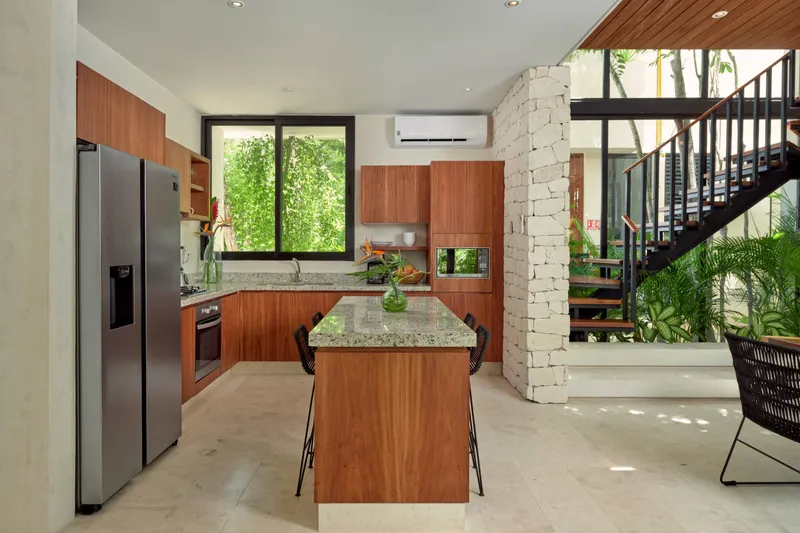 Casa Lucas kitchen with a wooden island bar and black stools, a stainless steel refrigerator and a stone column beside the open staircase