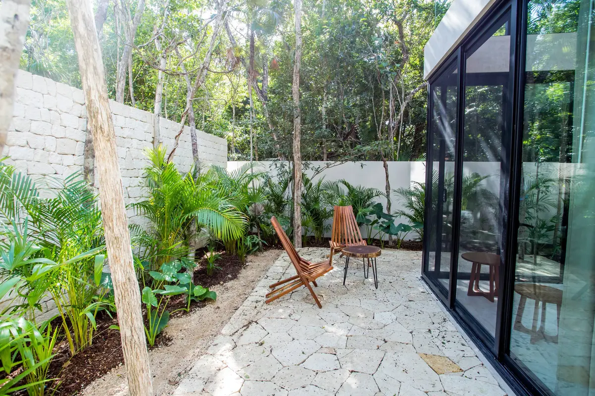 Casa Lucas loft patio with two wooden folding chairs and a round side table on the stone paving beside the loft's glass sliding doors, with palms along a dry stone wall