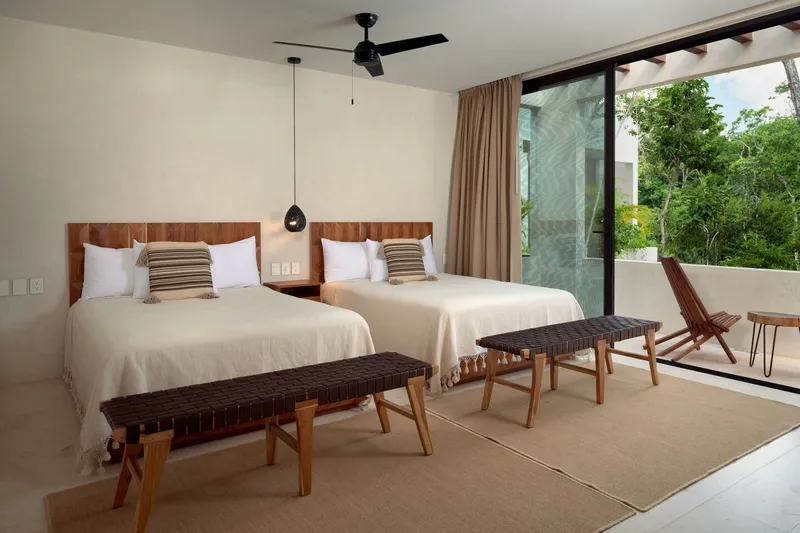 Casa Lydia guest bedroom with two beds, woven benches at the foot of each bed and a sliding door open to a terrace