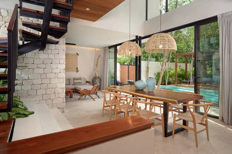 Casa Lydia dining table with wishbone chairs and woven pendant lamps beside glass doors onto the pool