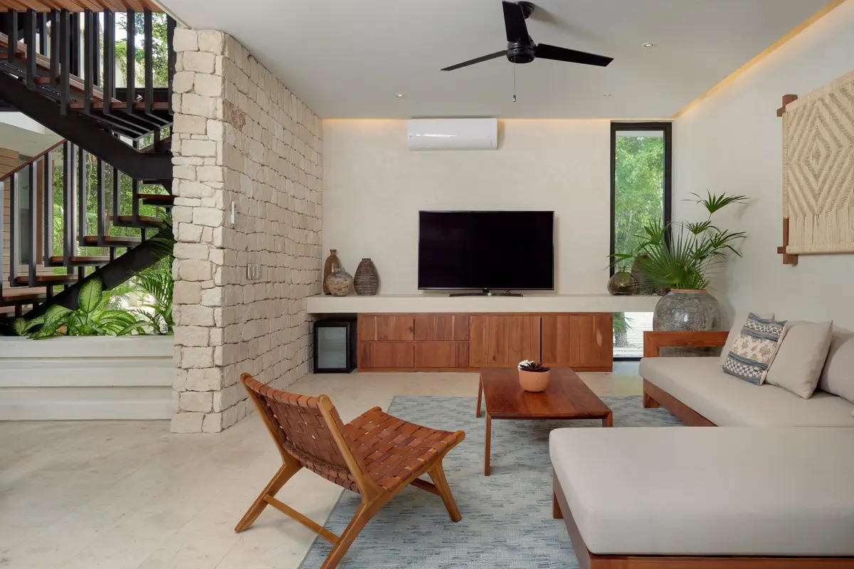 Casa Lydia living room with a stone wall, staircase, wall mounted TV, sofa and woven leather chair