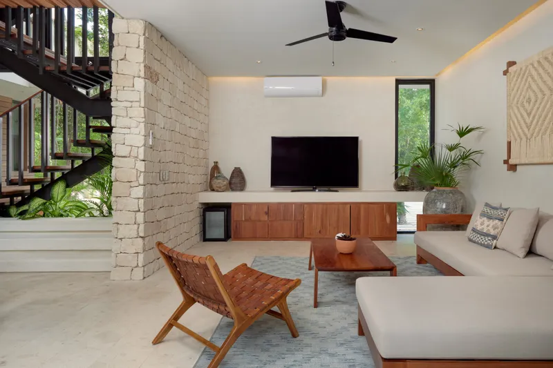 Casa Lydia living room with a stone wall, staircase, wall mounted TV, sofa and woven leather chair
