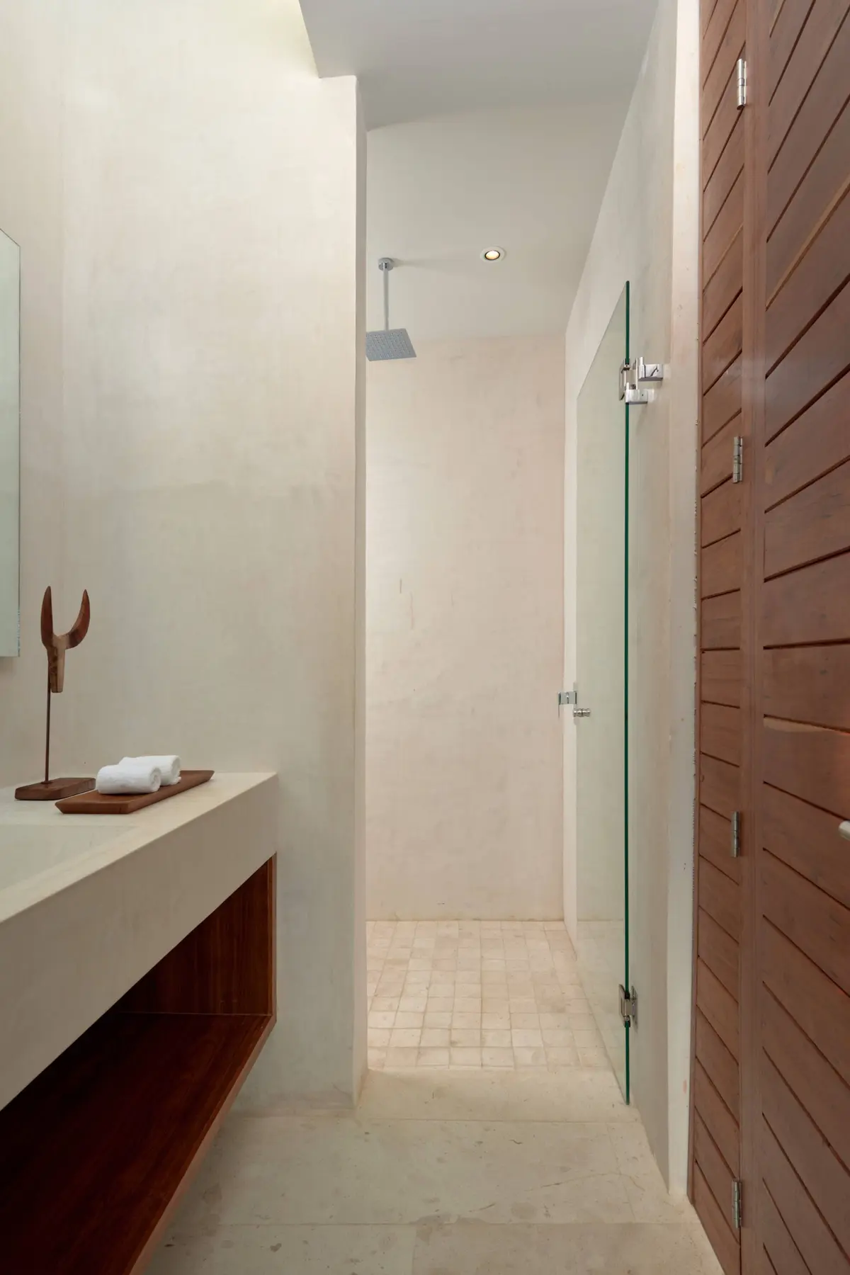 Casa Lydia master bathroom with a stone vanity, a rain shower behind a glass door and wooden slat doors