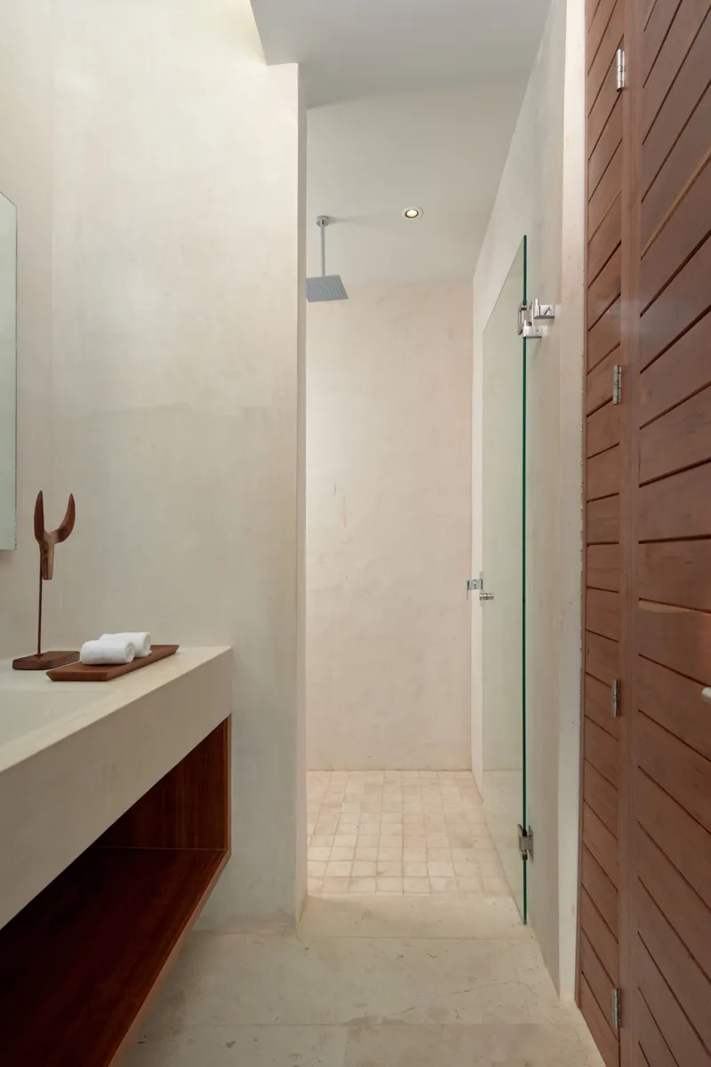 Casa Lydia master bathroom with a stone vanity, a rain shower behind a glass door and wooden slat doors