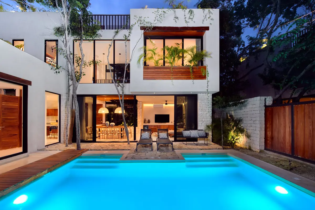 Casa Lydia pool lit at dusk with two loungers in front of the glass walled house