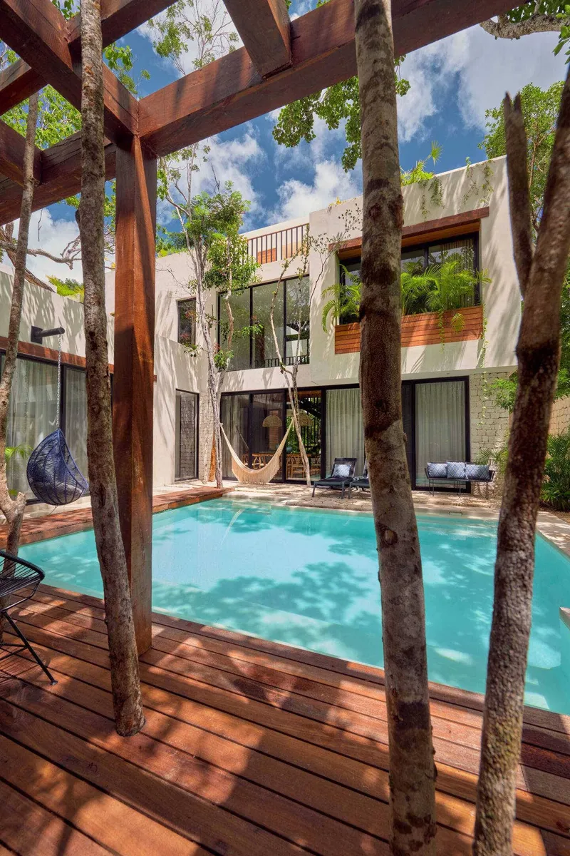 Casa Lydia pool seen from the wooden pergola deck with tree trunks and the house behind
