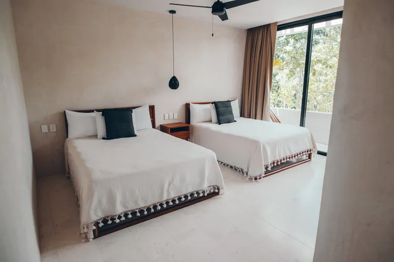Casa Thomas guest bedroom with two beds, dark grey pillows and a sliding door open to a terrace