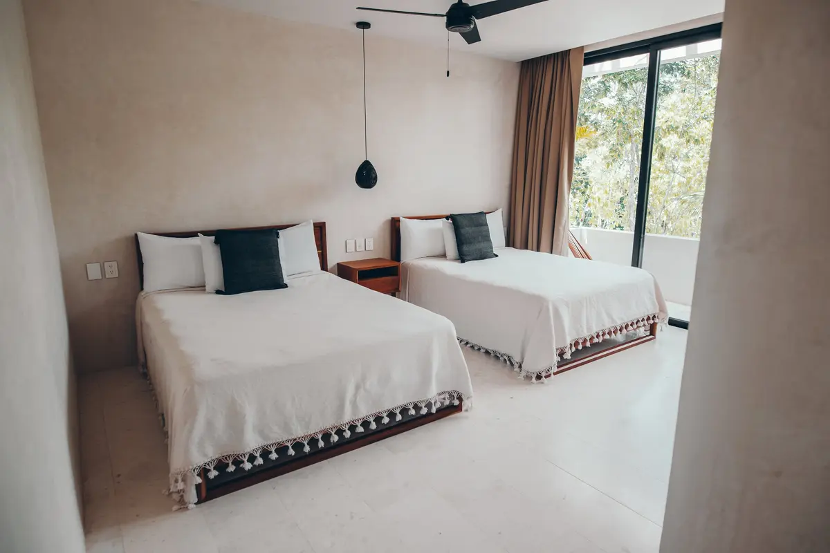 Casa Thomas guest bedroom with two beds, dark grey pillows and a sliding door open to a terrace
