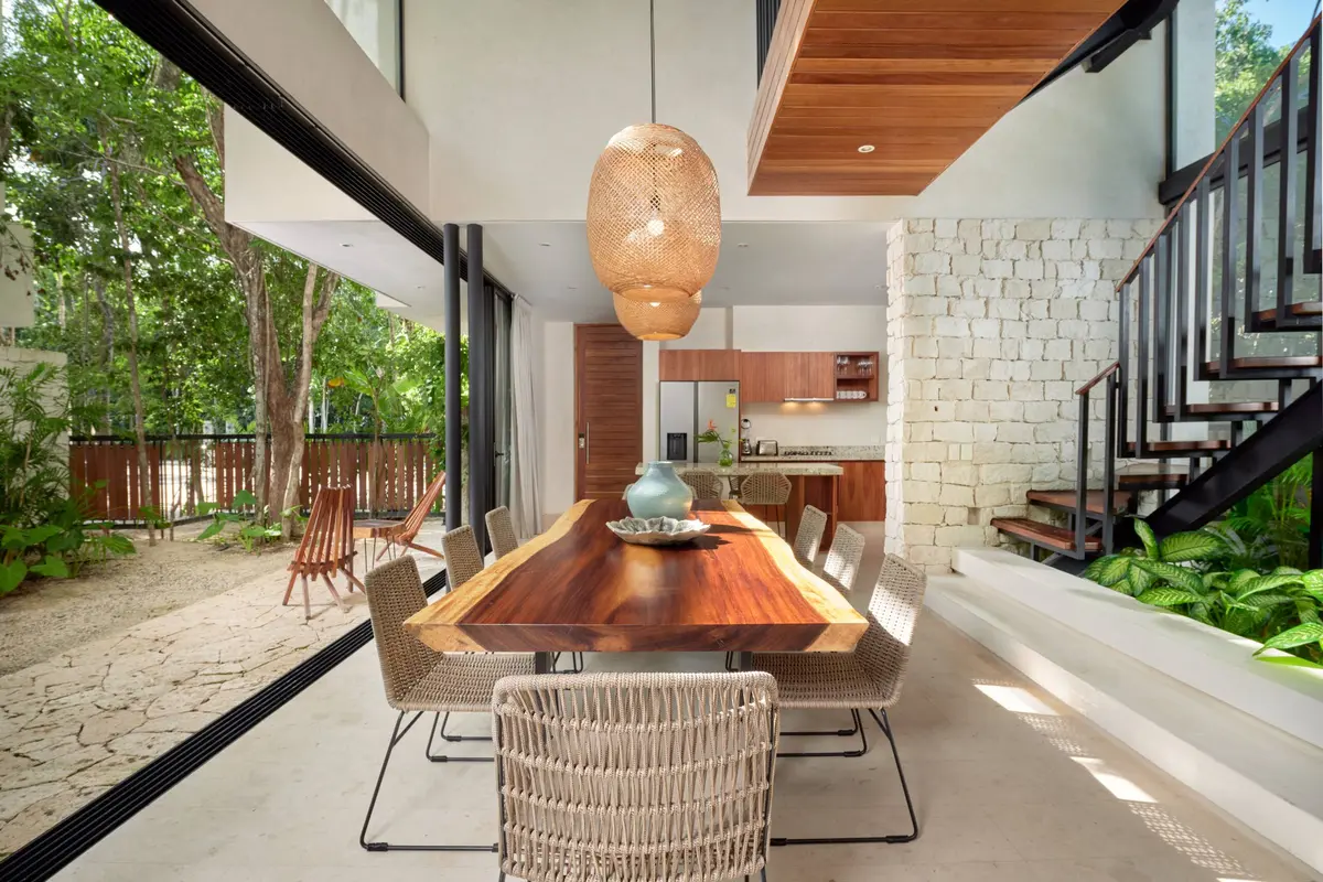 Casa Thomas dining room with a live edge wooden table, woven chairs and woven pendant lamps, open to the garden, with the kitchen behind