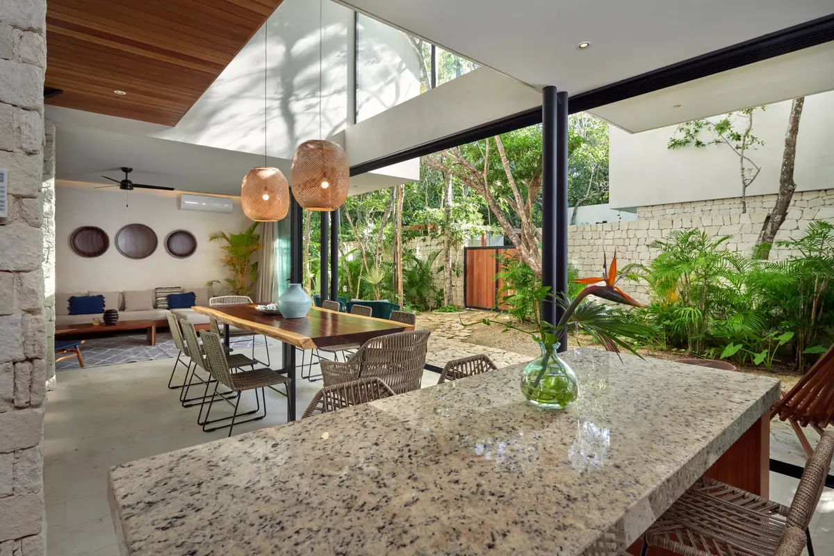 Casa Thomas kitchen counter with bar stools, a dining table with rope chairs and glass walls onto the garden