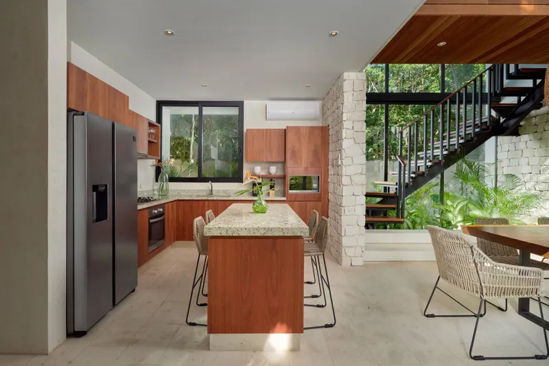 Casa Thomas kitchen with a granite topped island bar, woven stools, wooden cabinets and a stone column beside the open staircase