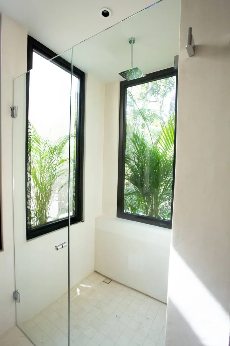 Casa Thomas master bathroom shower with a glass door, a square rain shower head and two tall windows onto palms