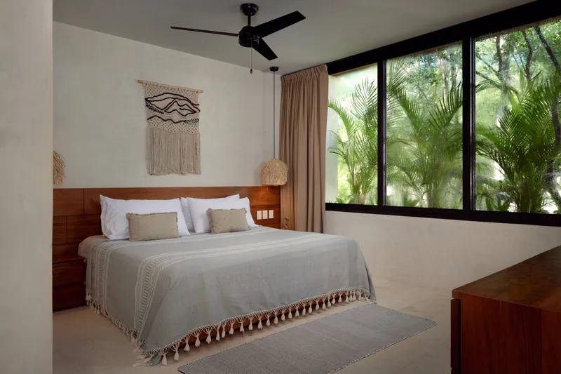 Casa Thomas master bedroom with a king bed, a macrame wall hanging, a ceiling fan and windows onto the jungle