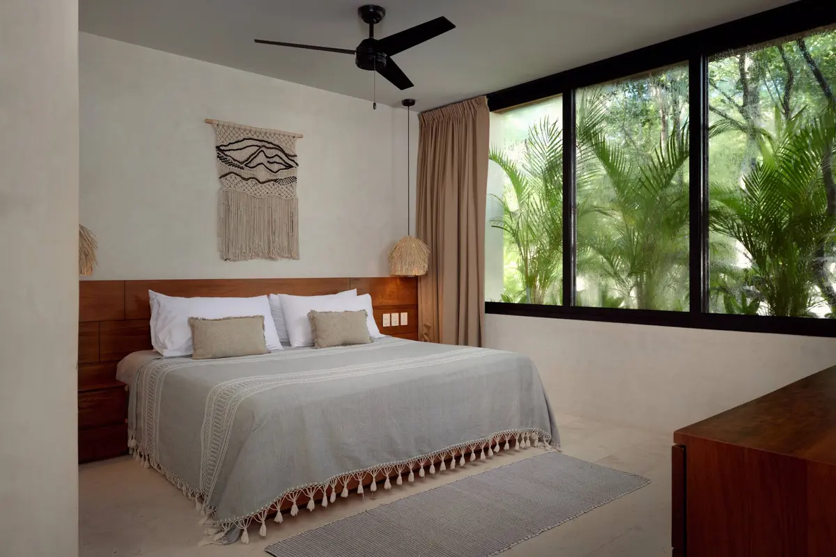 Casa Thomas master bedroom with a king bed, a macrame wall hanging, a ceiling fan and windows onto the jungle