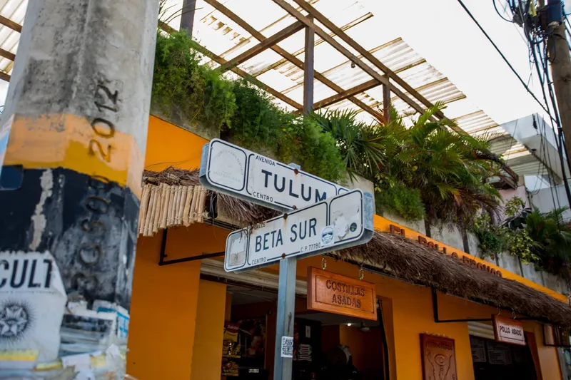 Downtown Tulum: the street signs of Avenida Tulum and Calle Beta Sur in front of an orange restaurant front with a palm thatch awning