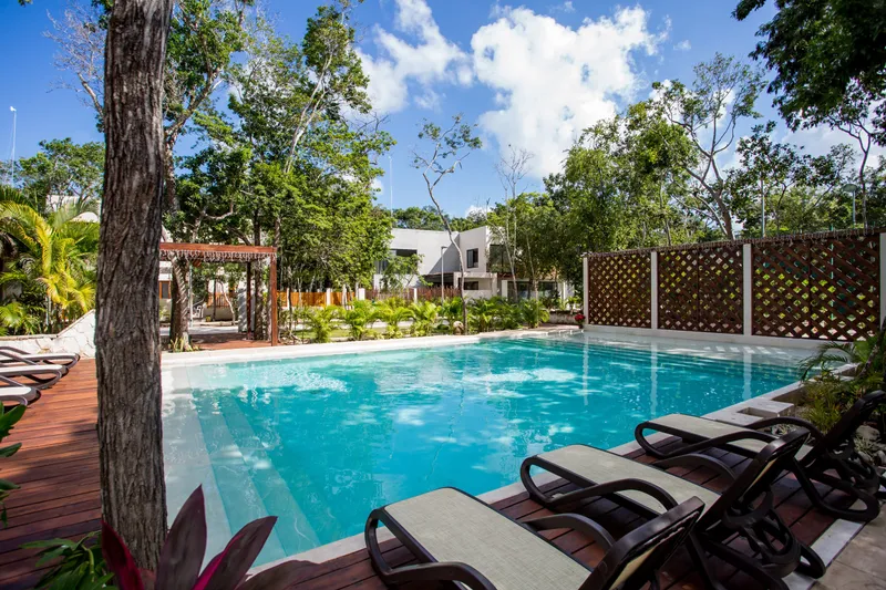 La Privada community pool: turquoise water with wide entry steps, sun loungers on a wooden deck, a pergola and white houses among jungle trees