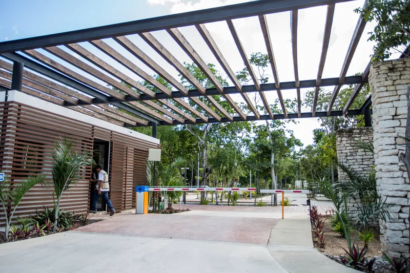 La Privada entrance: the security booth under a wooden pergola, a guard at the booth, red and white barrier arms across the road and jungle trees beyond