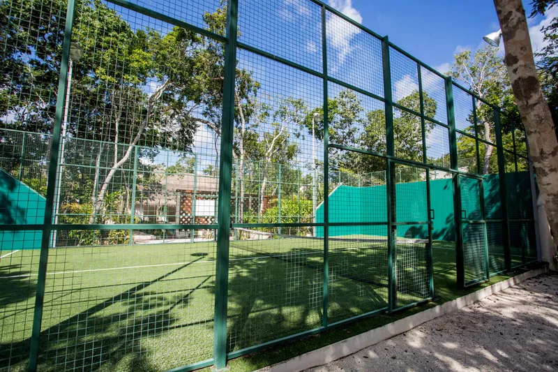 La Privada paddle tennis court: green artificial turf and a net behind a green mesh fence, among jungle trees