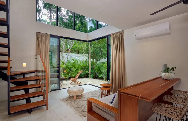 The loft living area, with an open wooden stair, a sofa, a wooden bar with woven stools and glass doors open onto a walled garden patio