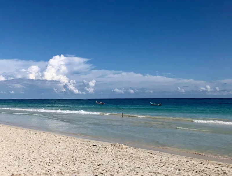 Tulum beach: white sand and turquoise water, with two small boats offshore under a blue sky