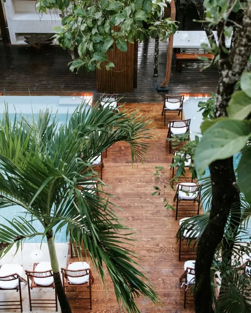 A wedding ceremony set up at Aldea Kaan Tulum: rows of wooden chairs with white cushions along a wooden aisle between palms