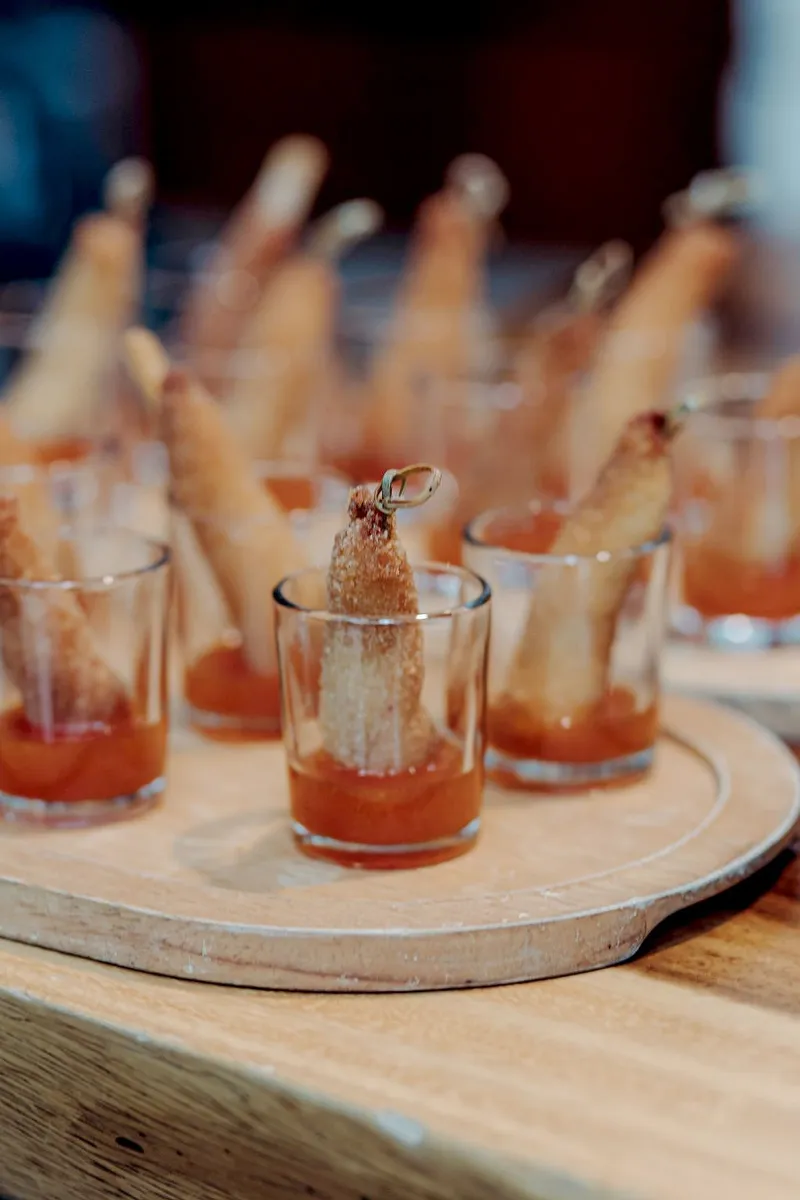 Appetizers at a wedding at Aldea Kaan Tulum: crumbed rolls standing in red sauce in shot glasses on a round wooden board