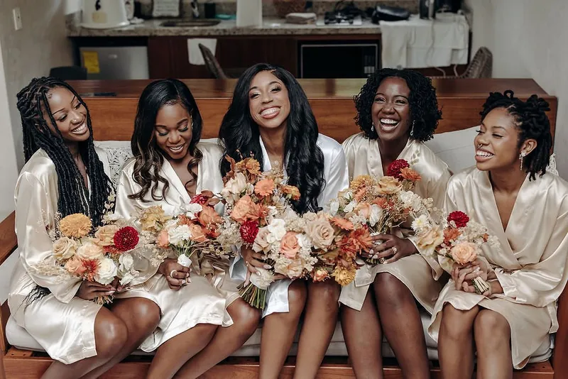 A bridal party getting ready at Aldea Kaan Tulum: five women in satin robes holding peach and orange bouquets on a sofa