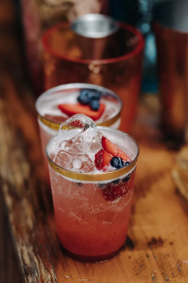 Cocktails at a wedding at Aldea Kaan Tulum: crushed ice, strawberries and blueberries in gold rimmed glasses beside a copper shaker
