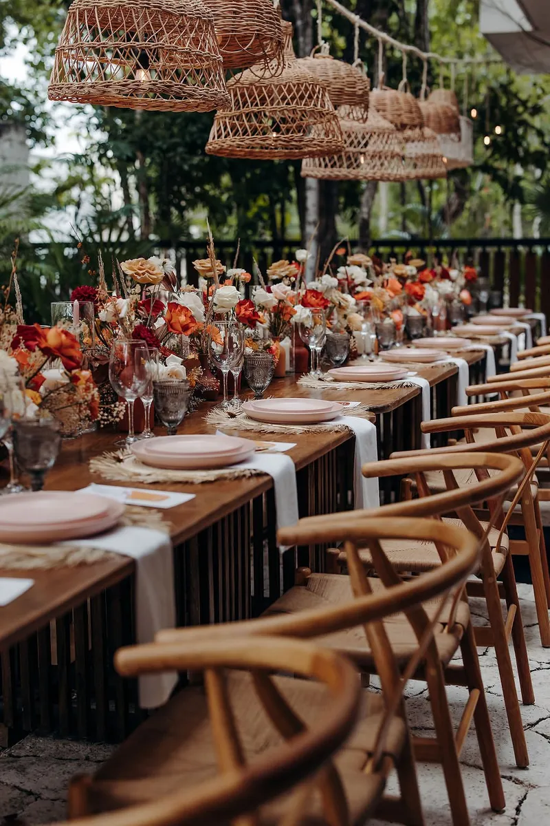 Wishbone chairs along a wedding dinner table at Aldea Kaan Tulum, with pink plates, white napkins and flowers under rattan lamps