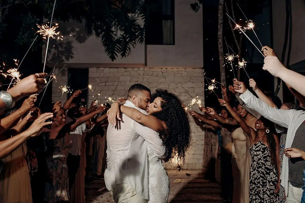 A couple kissing at night at Aldea Kaan Tulum between two rows of wedding guests holding sparklers
